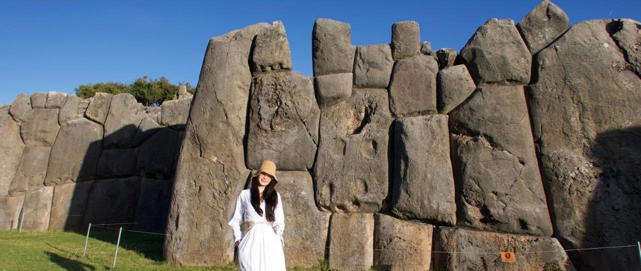 Traveler standing in front of the stone walls of Saqsayhuamán archaeological site in Cusco.