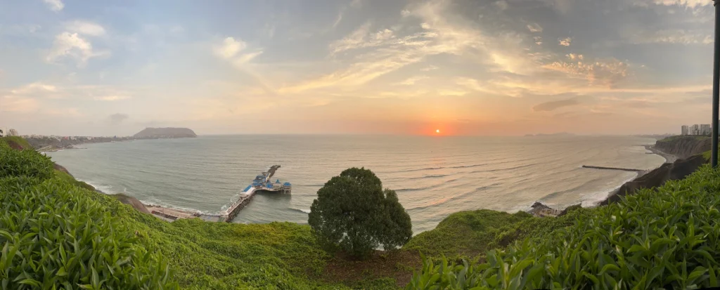 Panoramic view of the Lima Malecón overlooking cliffs, Pacific Ocean, and sunset skyline.
