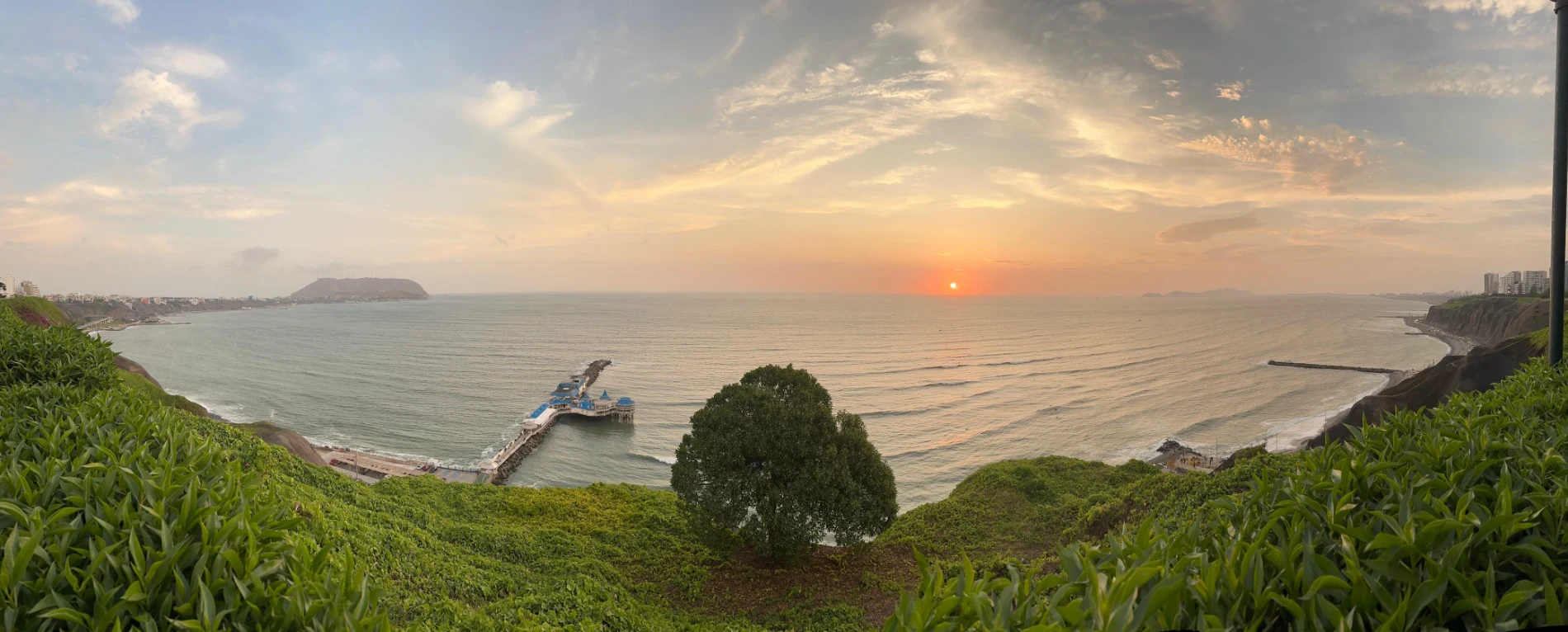 Panoramic view of the Lima Malecón overlooking cliffs, Pacific Ocean, and sunset skyline.