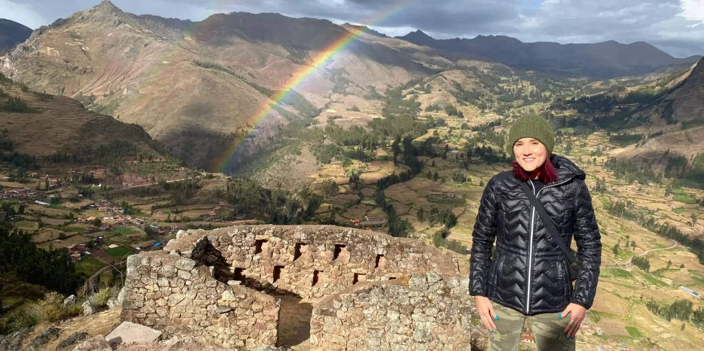 Angie Pon at the Pisac ruins with a rainbow in the background, symbolizing LGBTQ travel in Peru