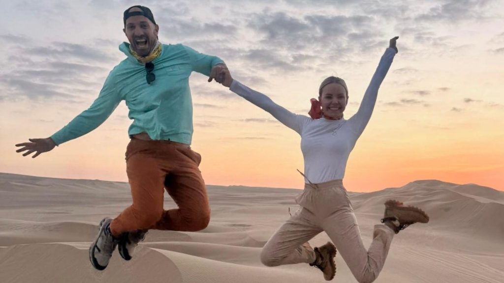 Couples luxury desert adventure jumping over golden sand dunes at sunset in Huacachina Peru