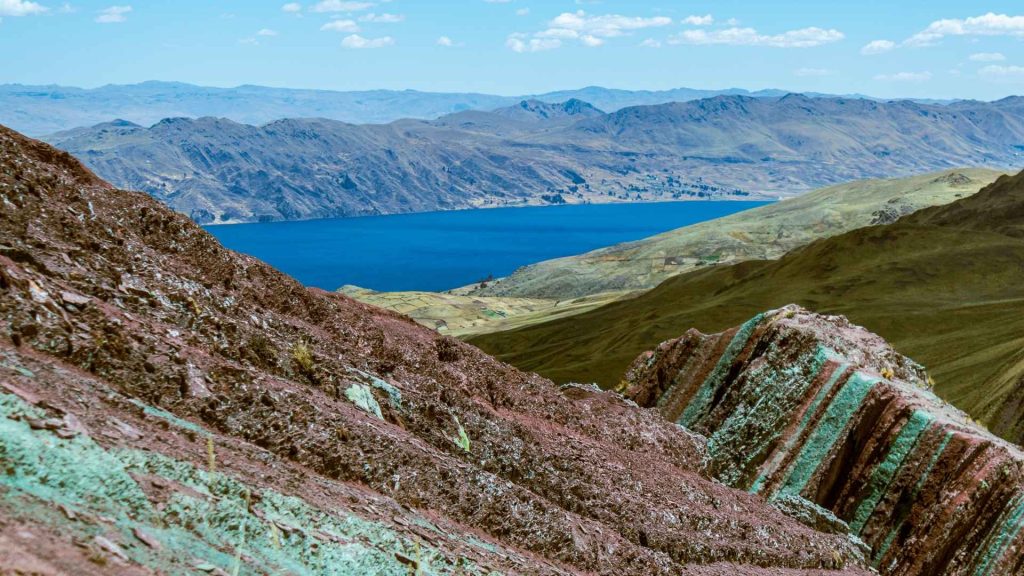 Panoramic view of mineral-rich red mountain ridges and a deep blue alpine lake on a custom Peru day trek